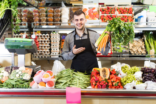 Man seller 20-29 years old is displaying assortment of grocery shop.