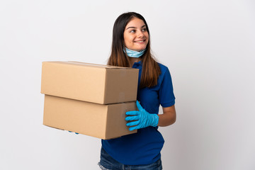 Young delivery woman protecting from the coronavirus with a mask isolated on white background looking up while smiling