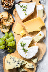 Assorted cheeses on a wooden cutting Board. Camembert, brie, Parmesan and blue cheese with grapes...