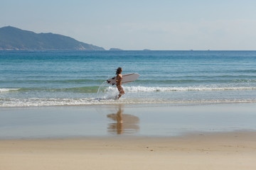 young beautiful girl in a swimsuit with a surfboard in her hands on the beach near the water, sea, summer, heat, sunny day, clear sea water, wave, lifestyle, sport, leisure, vacation, day off,