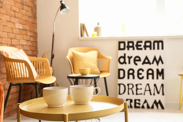 Stylish interior of living room with table and cups
