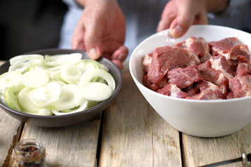 Selective focus. Chef's hands are preparing meat kebab with onions. A bowl of raw meat and a bowl of onions. Barbecue cooking.