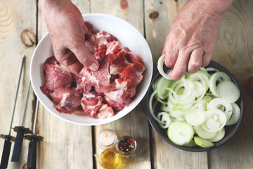 Selective focus. Chef's hands are preparing meat kebab with onions. A bowl of raw meat and a bowl of onions. Barbecue cooking.