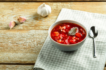 A plate of borscht with chicken on a napkin with a spoon on a wooden table.