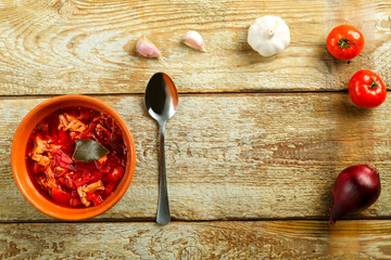 A plate of clay borscht with chicken with a spoon on a wooden table near vegetables.