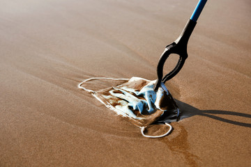 collecting a used surgical mask on the beach