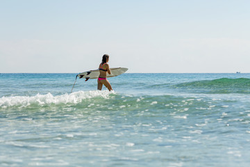 a girl with a surfboard enters the sea, summer, sunny day, clear water