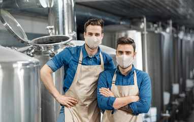 Fototapeta na wymiar Two men in aprons and protective masks stand near equipment and kettles