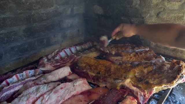 Man hands moving around pieces of beef meat in Argentinian asado to cook evenly