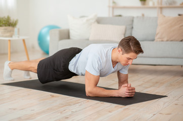 Young man go in for sport at home. Athlete doing plank on mat