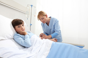 Obraz premium Nurse medicating sick and afraid child lying in bed in hospital room and getting him the drip