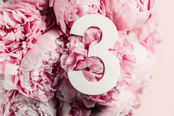 Creative layout. Pink peony flowers and digit three 3. Birthday greeting card. Anniversary concept. Top view. Copy space. Stylish white numeral over flowers background. Numerical digit.