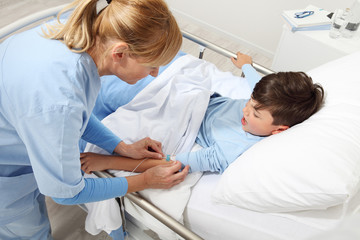 Fototapeta premium Up view of nurse medicating sick child lying in bed in hospital room and getting him the drip