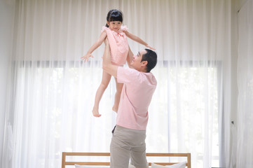 A healthy father is holding happy cute daughter flying and playing plane together at home on weekends, family concept.