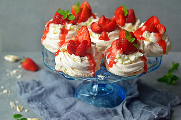 Meringue nests with strawberries on a glass plateau, over a stone gray background