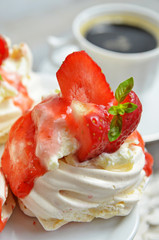 Little meringue with strawberries on a white background. Coffee cup in the background