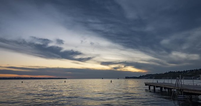 Time lapse of dramatic and colorful sunset over concrete pier and small town Portoroz in Slovenia. Adriatic Sea in summer. People taking photos. Wide shot, zoom out, 4K