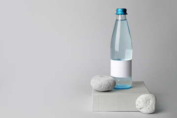 Bottle of clean water and pebbles on light background