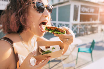 Happy woman eats a fast food flatbread with filling sitting on the street and resting after a working day. Concept of healthy food and extra calories