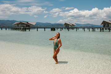 Young slim tourist woman enjoy suntan, standing in the tourquise water in front of wooden owrwater...