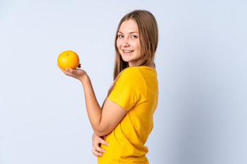 Teenager Ukrainian girl isolated on blue background holding an orange