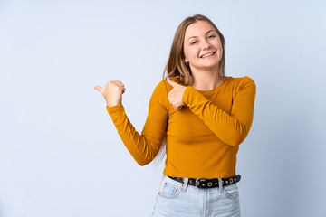 Teenager Ukrainian girl isolated on blue background pointing to the side to present a product