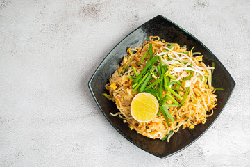 Pad Thai served with lemon slices in black dish on gray cement background
