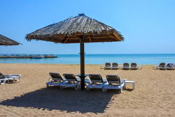 Shaded recliners under thatched roof near calm tropical blue waters of the Persian Gulf 