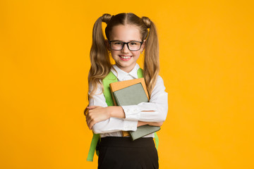 Smiling Elementary Student Girl Hugging Books On Yellow Studio Background