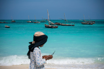 Young local girl on the beach with Turquoise Water and Dhow Boats in Ocean in Nungwi, Zanzibar, Tanzania
