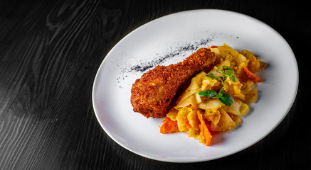 Roasted chicken leg and vegetables in white plate on black wooden table background