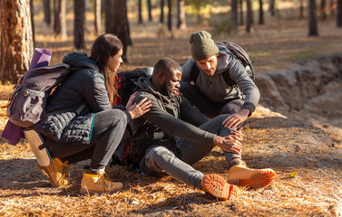 Friends helping black guy with injured leg, hiking at forest