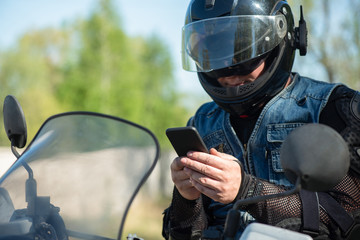 Motor biker with a mobile phone in hands close up.