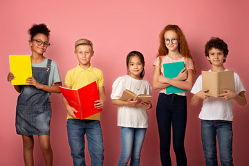 Portrait of multiethnic kids with textbooks and notebooks ready to start new school year over pink background