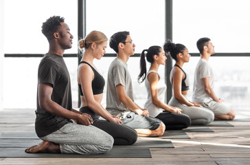 Happy multiracial men and woman practicing yoga and meditating together in studio