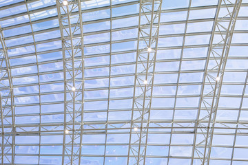 Metal structure supporting a glass dome, texture background. Transparent glass ceiling, sunlight and blue sky. The architecture of a modern trendy building with natural lighting.