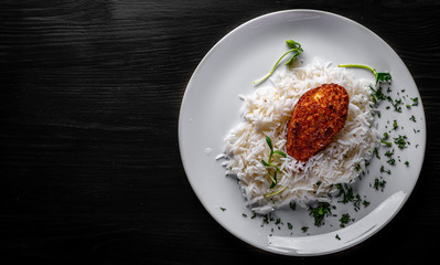roasted burger with rice in white plate on black wooden table background