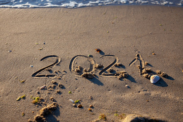 The numbers 2021 are written in the sand. New year on the beach. Sea coast, wave. Natural background. Place for your text. Summer in winter.