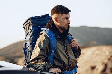 Portrait of a young traveler man in hiking equipment standing near his off-road car