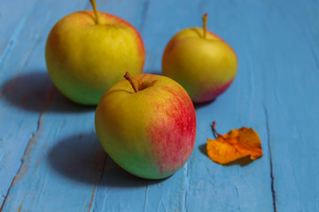 Three fresh apples lie on a table of wood, beside one small leaf