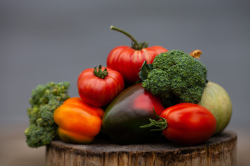 Fototapeta na wymiar Bright colorful vegetables on a grey concrete background. Fresh organic vegetables (broccoli, tomatoes, pumpkin, peppers) from the garden on a wooden stump. Autumn concept, thanksgiving day, harvest.