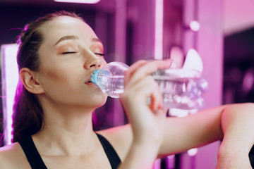 Young sporty woman drinking water in a gym