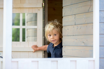 Sweet toddler boy, playing in wooden doll house in garden