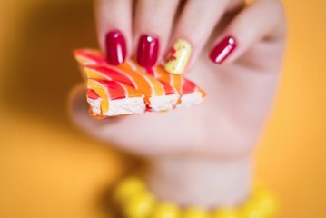 a woman's hand with a bright manicure holds a piece of multicolored dessert