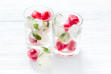 Cocktail glasses with berries in ice cubes on white table