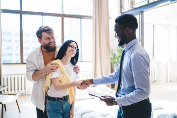 Black realtor greeting happy couple in apartment