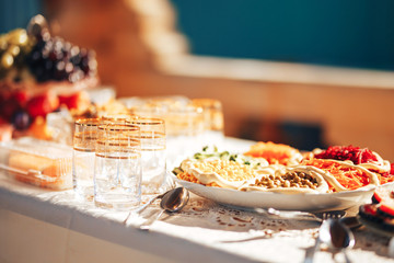 Long table covered with a tablecloth on which there is a lot of food, food in plates