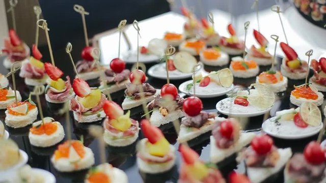 Shooting near various types of delicious types of appetizers on skewers for guests at wedding party lying on black table of banquet hall in the morning. Delicious appetizers in front of main course.