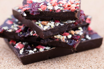 Handmade bitter chocolate with berries and green pistachios on a cork wood background. Macro photography of food. A close-up of a broken chocolate.