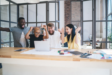 Group of elated multiethnic coworkers using laptop at office